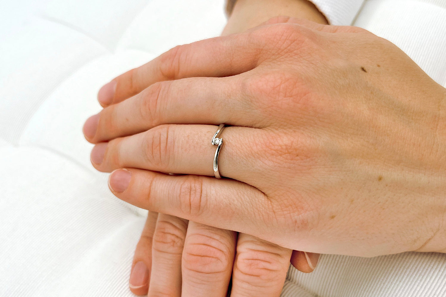 Geschwungener Spannring aus Weißgold mit 0,05ct Solitär Diamant an einer Frauenhand getragen