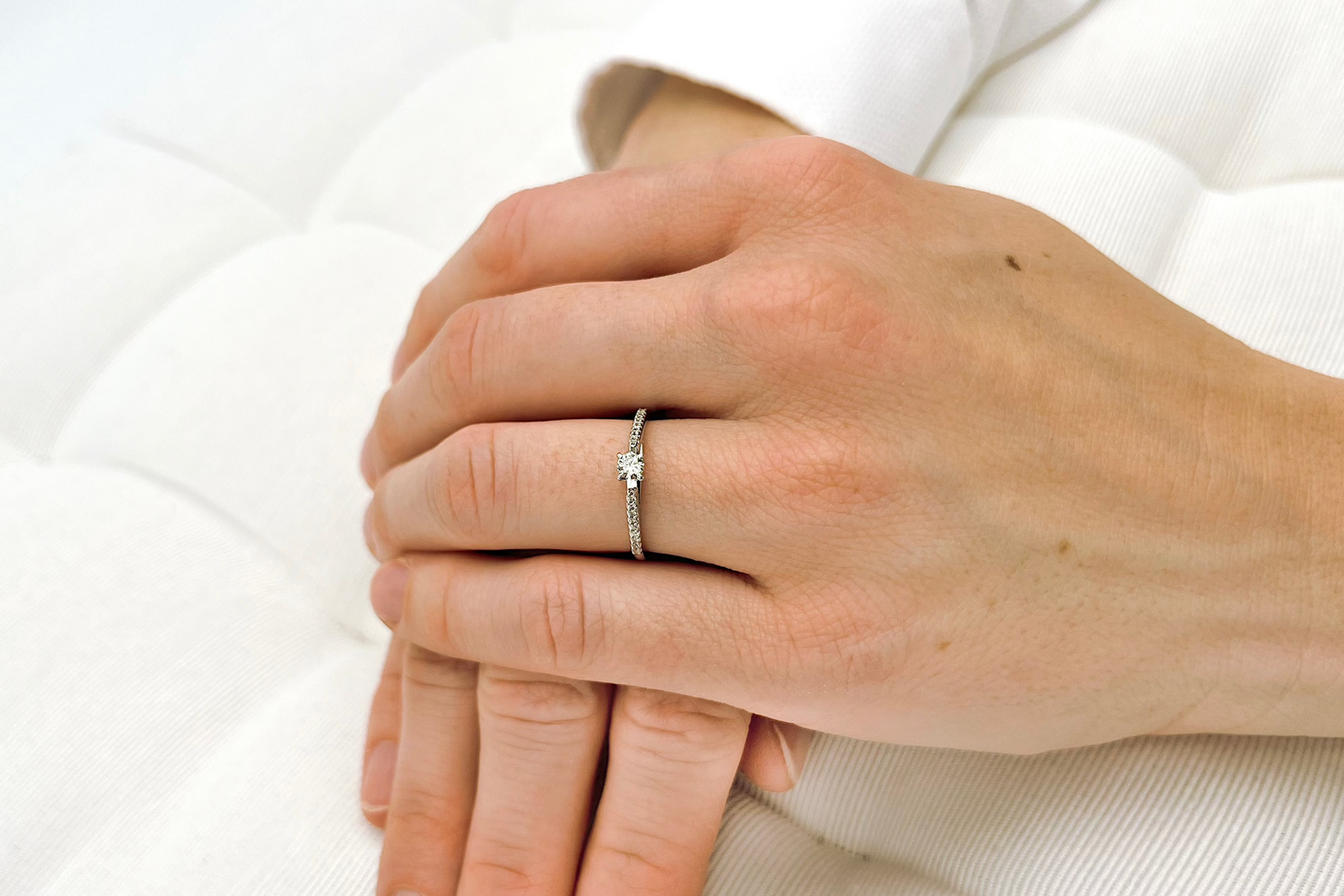 Ein Verlobungsring mit Solitärdiamant und Pavé gefassten kleinen Diamanten aus Weißgold an Frauenhand